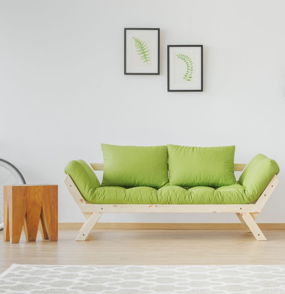 Sillón verde con dos cuadros en una pared blanca.